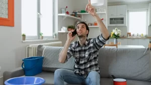 man on phone checking ceiling leak with buckets