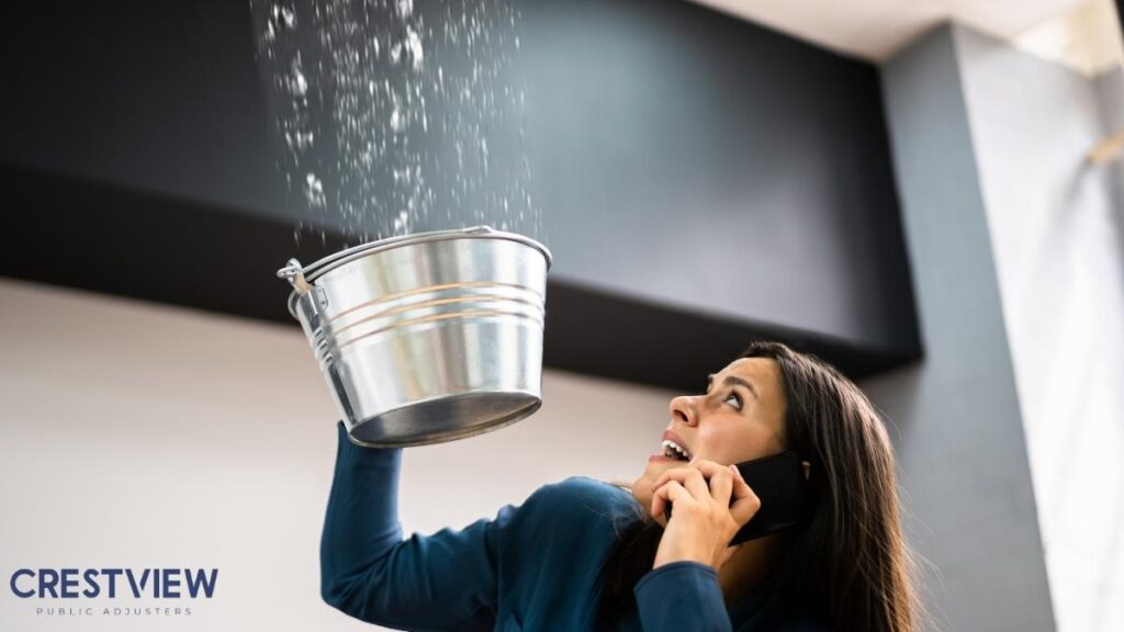 Commercial Water Damage Claim In New Jersey: Why Business Owners Should Work With A Public Adjuster 2 Business owner holding a bucket under a ceiling leak while calling for help
